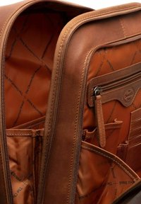 Interno di una borsa in pelle marrone con scomparti con cerniera, rivestimento in tessuto con logo del marchio e diversi taschini per l'organizzazione.