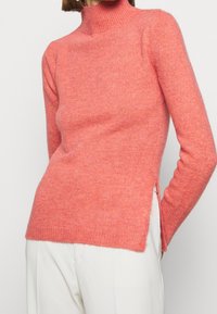 Maglione a collo alto color rosa, realizzato in morbido tessuto a maglia, con un design aderente, polsini a coste e spacchi laterali per facilitare i movimenti.