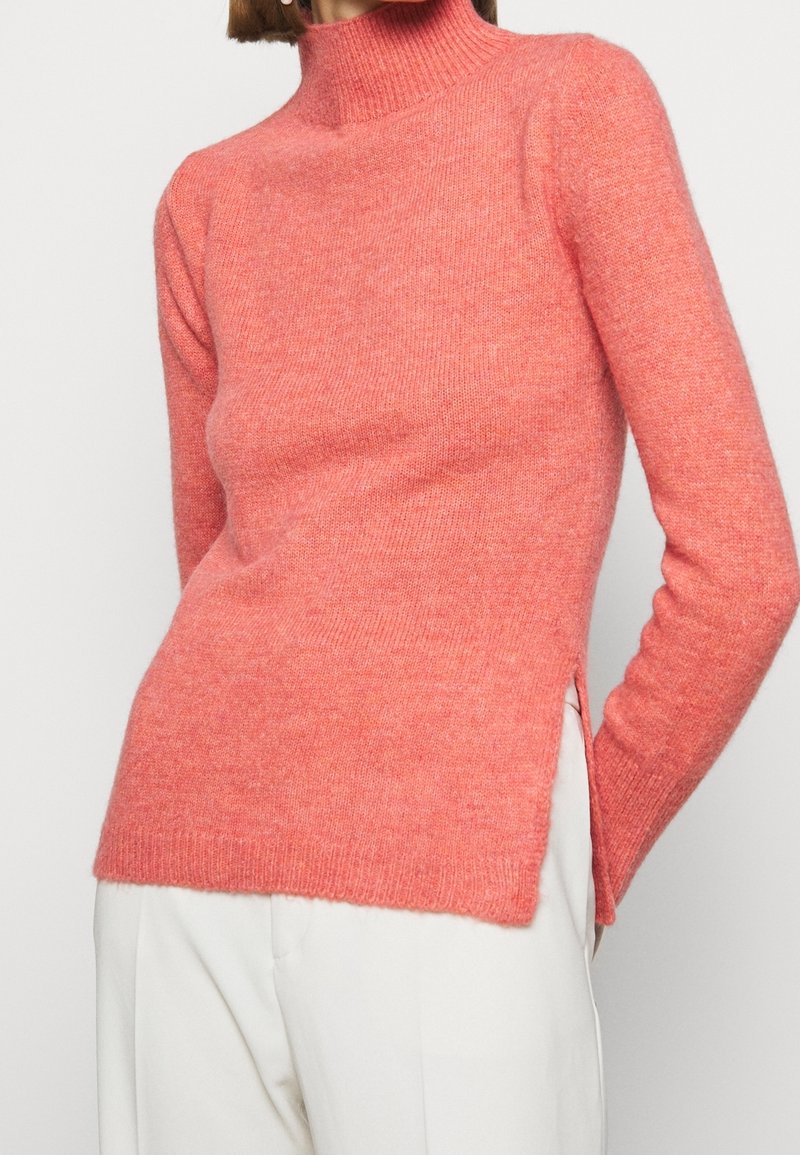 Maglione a collo alto color rosa, realizzato in morbido tessuto a maglia, con un design aderente, polsini a coste e spacchi laterali per facilitare i movimenti.