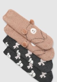 Tre paia di calzini pelosi: uno beige con la faccia di un orso e pompon, uno nero con motivi di ossa bianche e un terzo con dettagli grigi.