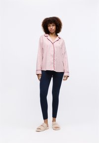 Pajamablus i ljusrosa med marinblå piping, långa ärmar och knäppning fram; matchad med marinblå leggings och beige fluffiga tofflor.