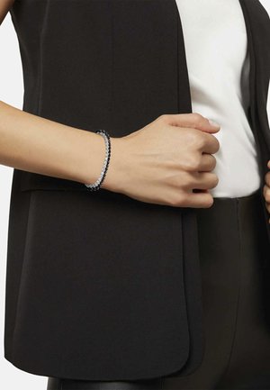 Czarny i srebrny bransoletka z na przemian ułożonymi koralikami, noszona na nadgarstku, w połączeniu z czarną kamizelką i białą bluzką. Gładka tekstura i elegancki design.