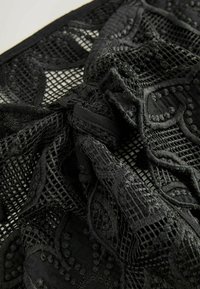 Tissu en dentelle noire avec broderie florale et motif en mesh torsadé en un nœud, montrant des textures détaillées et un travail délicat.