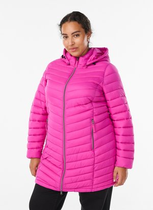 Femme portant un manteau d'hiver matelassé à capuche rose vif, avec une fermeture éclair frontale et des poches latérales zippées, debout sur un fond blanc.