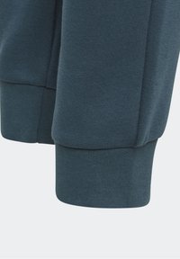 Mörk teal sweatshirtärm med ribbad mudd. Texturerad tyg visar en mjuk, stickad design. Sömnadsdetaljer är synliga nära muddens kant.