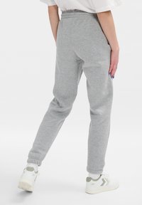 Grijze sweatpants met een zachte textuur, elastische tailleband, taps toelopend ontwerp en enkels waarin cuffs zijn, gecombineerd met witte sneakers met groene accenten.