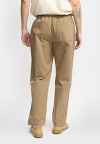 Beige katoenen broek met een relaxte pasvorm, elastische tailleband en een achterzak. Eenvoudige textuur en minimalistisch ontwerp.