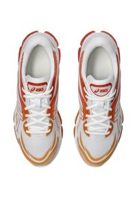 Sneakers bianchi e arancioni con tessuto a rete, design curvo, logo in evidenza e lacci. Presentano una suola texturizzata e accenti a forma di fiamma.