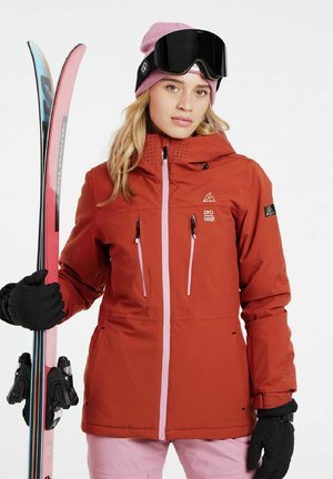 Red ski jacket with pink accents, zippered pockets, and textured hood. Black gloves, pink ski pants, and skis with pink and blue detailing.
