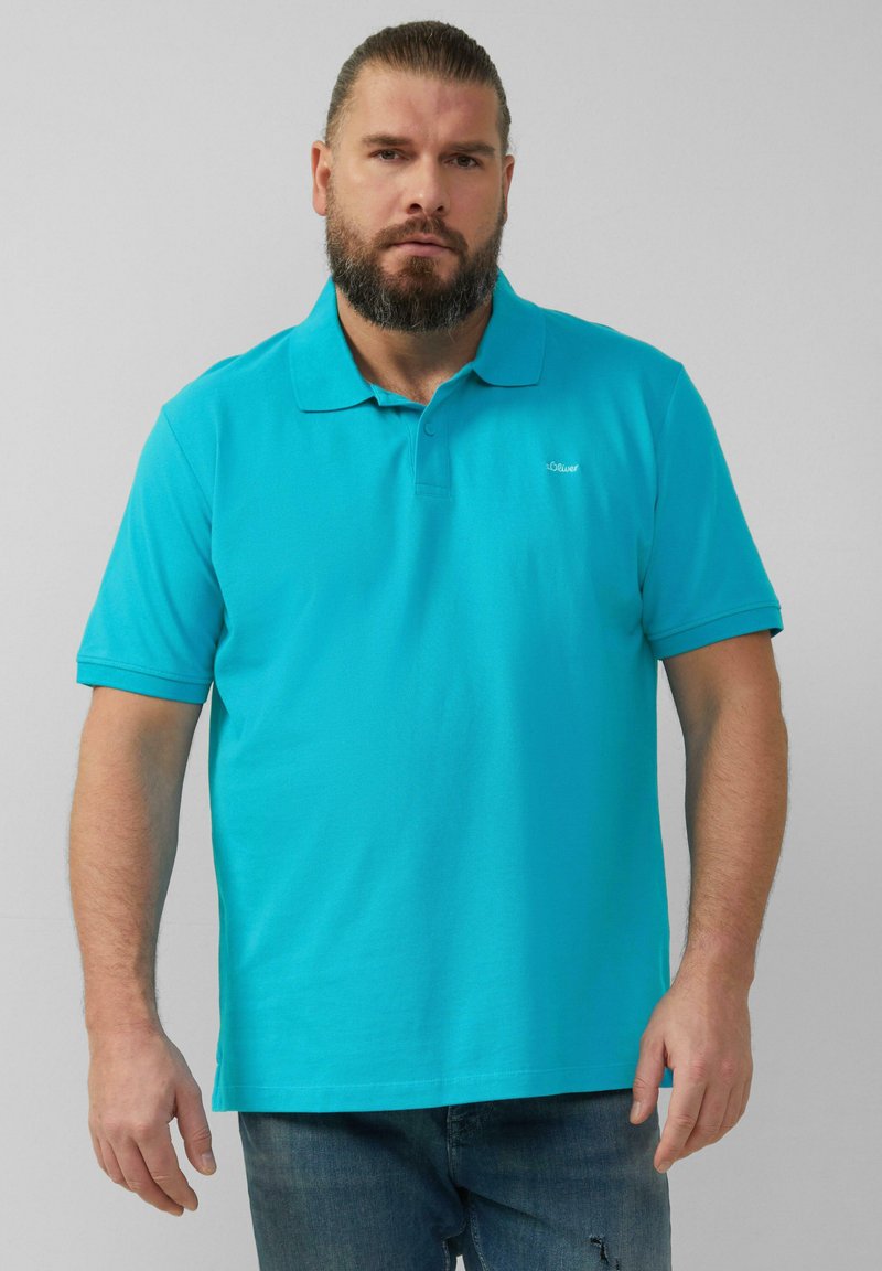 Türkises Poloshirt aus Baumwolle mit klassischem Kragen-Design. Mit kurzen Ärmeln und einem dezenten Logo auf der Brust. Getragen mit blauer Jeans.