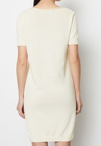 Abito in maglia di colore crema, di lunghezza media con maniche corte, caratterizzato da un collo rotondo e orli a coste in fondo e alle maniche. Texture liscia.