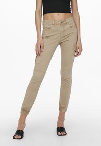 Beige cargo pants with elastic cuffs, featuring multiple side pockets, a fitted design, and smooth cotton fabric.