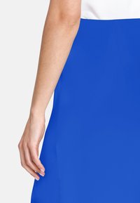 Blå kjol med en mjuk, texturerad yta. Tyget verkar lätt och har en figurnära design med en enkel, ren silhuett.