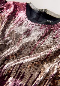 Top ar spīdumiem, kas attēlo gradientu no rozā, zelta un sudraba toņiem. Plakanie spīdumi veido gludu, atstarojošu virsmu ar apaļu kakla izgriezumu.