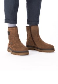 Bruine suède enkellaarzen met een zijrits, rubberen zool en gevoerde kraag; gestructureerd lijf en versterkte hak voor duurzaamheid.