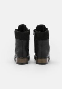 Bottines noires en cuir et daim, avec une doublure en peluche, fermeture éclair et talon en bois. Détail de logo remarquable sur le talon.
