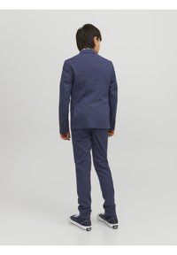 Granatowy garnitur o dopasowanym kroju, z jednozapięciową marynarką i dopasowanymi, wąskimi spodniami, w zestawieniu z białymi trampkami.