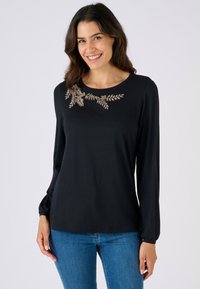 Maglietta nera a maniche lunghe con collo rotondo, caratterizzata da ricami floreali dorati sul petto e polsini elasticizzati. Tessuto morbido e liscio.