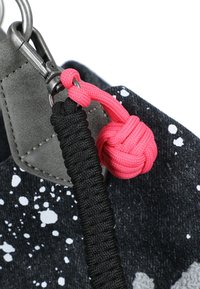 Portachiavi in paracord nero e rosa con nodo monkey fist attaccato a un clip in metallo e tessuto nero a pois.