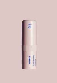 Il rossetto vellutato Korres True in un astuccio cilindrico di un pallido rosa con una presa rigata; presenta un testo blu che mostra il numero della tonalità e il nome del prodotto.