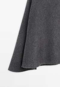 Tissu en laine grise avec une texture douce, présentant un tombé fluide et un ourlet légèrement arrondi pour un look élégant.