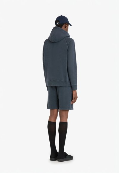 Un sweatshirt en coton bleu marine avec cordon de serrage, associé à un short en coton assorti. Le modèle porte des chaussettes noires montantes et des baskets.