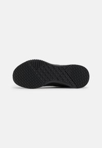 Suela de zapatilla negra con goma texturizada para agarre, que presenta un diseño de banda de rodadura con patrones y una sección de talón reforzada para mayor durabilidad.