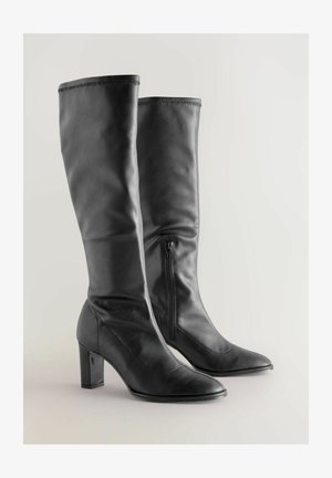 Svarta läderknähöga stövlar med spetsiga tår, blockklackar, subtil söm och sidodragkedjor för enkel påtagning. Slät textur.