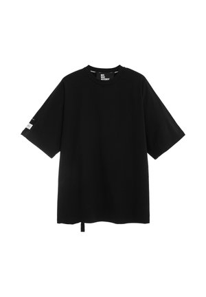 Camiseta negra de manga corta oversize con cuello redondo, pequeño texto blanco en el interior del cuello y detalle de una raya blanca en la manga izquierda.
