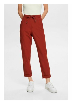 Röda skräddarsydda byxor med dragsko i midjan, uppvikt nederkant och sidofickor. Bärs med vita sneakers och en figurnära ljus topp.