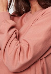 Sweat-shirt rose en tissu texturé et doux. Les manches sont légèrement froncées aux poignets et la coupe est ample.