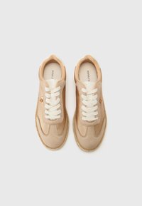 Beige sneakers med en teksturert semsket skinn- og læroverdel, hvite lisser, og en vevd jutesåle; gullfarget logo nær lisser.