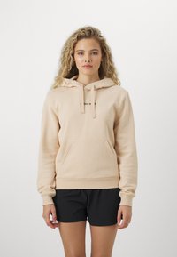 Felpa beige chiaro con tasca frontale, cappuccio con lacci e un piccolo logo stampato in nero. Il tessuto appare morbido e presenta una superficie liscia.