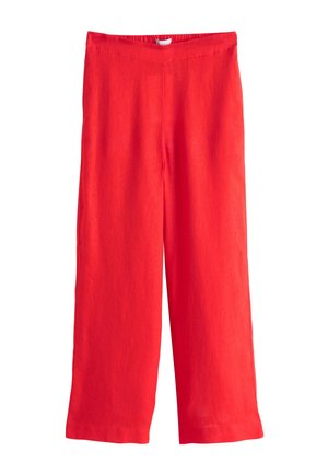 Zbliżenie osoby noszącej czerwone spodnie z ręką w kieszeni i białą koszulą częściowo wpuszczoną do środka.