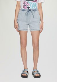 Jasnoniebieskie szorty dżinsowe z elastycznym pasem i sznurkiem. Posiadają podwinięte nogawki i kieszenie boczne. W zestawie z niebieskimi sandałami na podwójnych klamrach.