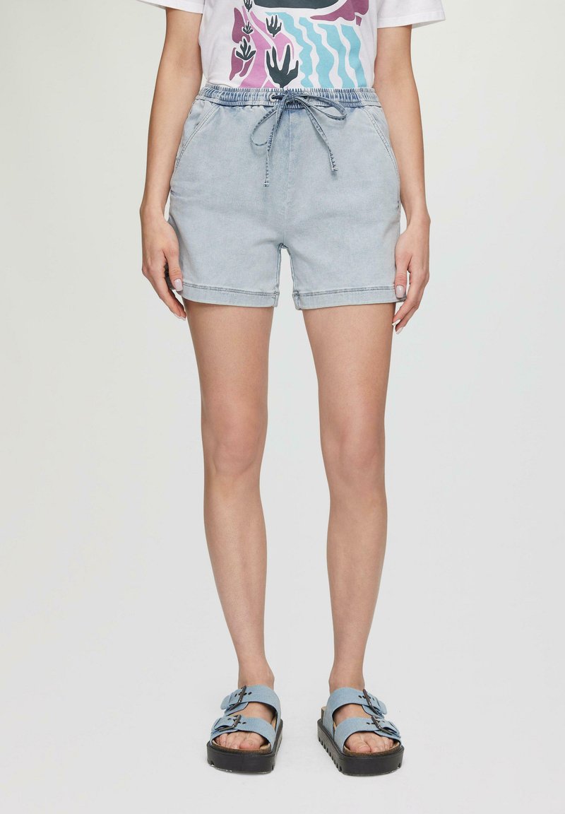 Jasnoniebieskie szorty dżinsowe z elastycznym pasem i sznurkiem. Posiadają podwinięte nogawki i kieszenie boczne. W zestawie z niebieskimi sandałami na podwójnych klamrach.