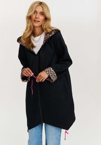 Černý plášť s kapucí s podšívkou a manžetami z leopardího vzoru. Obsahuje zipový přední uzávěr a růžové šňůrky na spodním okraji. Měkká textura látky.