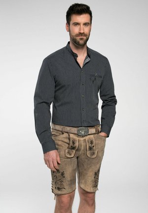 Herrenoutfit mit einem dunkel gestreiften Langarmhemd und lichtbraunen Ledershorts mit floraler Stickerei und einer dekorativen Gürtelschnalle.