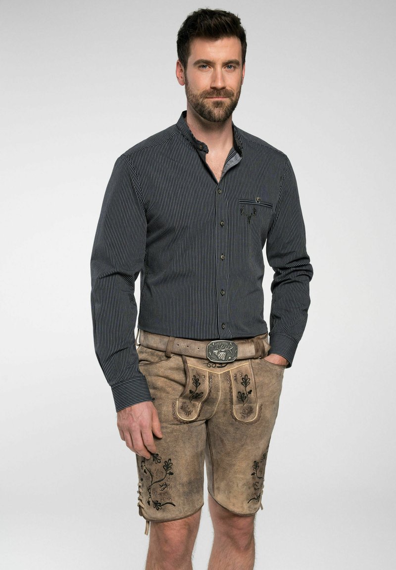 Herenoutfit met een donker gestreepte lange mouw shirt en lichtbruine leren shorts met bloemenborduring en een decoratieve riemgesp.