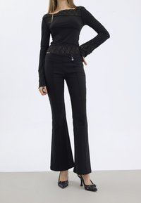 Svart långärmad topp med spetsdetaljer och utsvängda svarta byxor. Outfiten har en figurnära design, mjuk textur och en subtil lyster.
