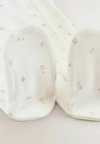 Biały materiał z małymi wzorami kwiatowymi w kolorach różowym, zielonym i żółtym. Miękka, gładka faktura z zaokrąglonymi krawędziami i delikatną konstrukcją.