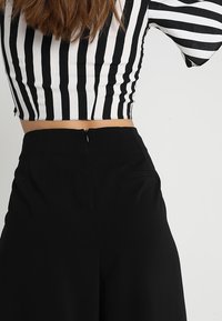 Černé kalhoty s vysokým pasem se skrytým zipem vzadu, doplněné o krátký černobílý proužkovaný top. Hladká texturovaná tkanina.