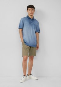 Niebieska koszulka polo w gradient, z kieszenią, krótkimi rękawami i kołnierzykiem. Połączona z beżowymi szortami i białymi trampkami. Gładka struktura materiału.