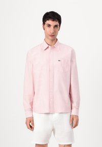 Rosa og hvit stripete skjorte med knapp-ned krage, brystlomme og brodert logo. Stoffet ser glatt og lett ut.