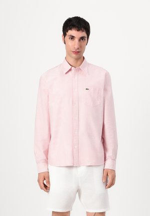 Chemise rayée rose et blanche avec un col boutonné, une poche poitrine et un logo brodé. Le tissu semble lisse et léger.