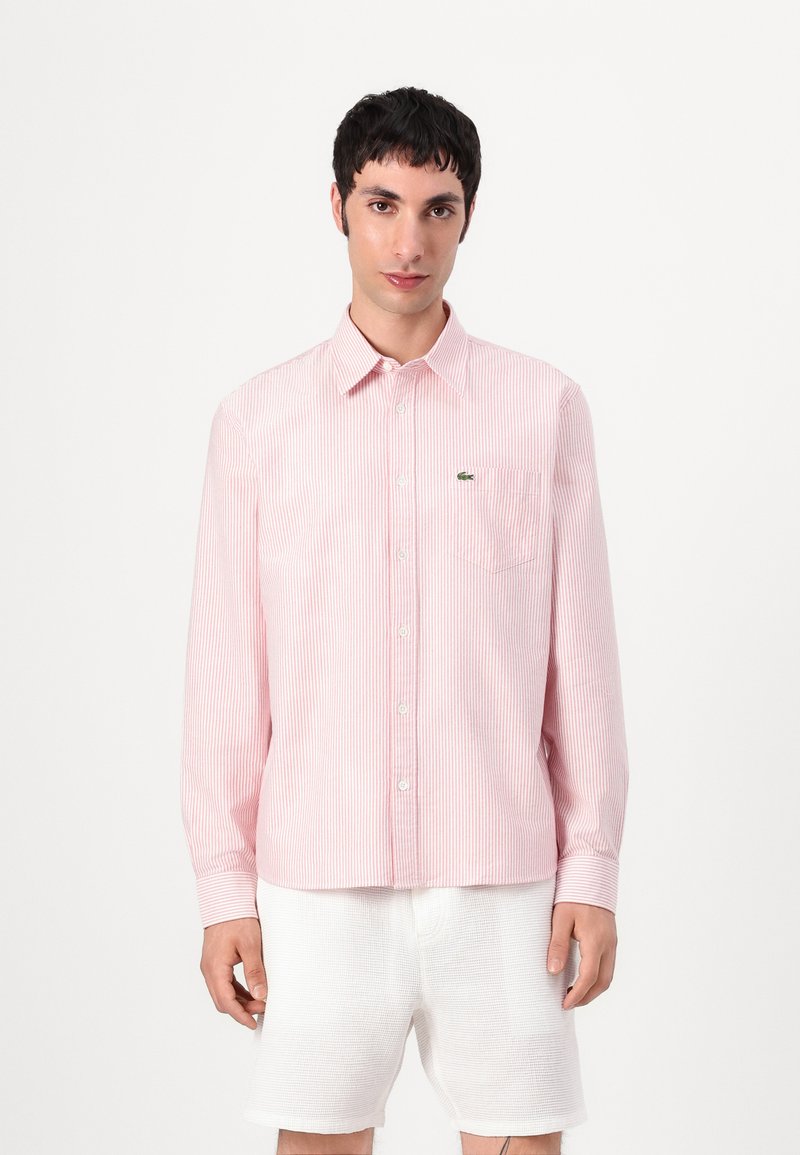 Rosa og hvit stripete skjorte med knapp-ned krage, brystlomme og brodert logo. Stoffet ser glatt og lett ut.