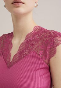 Top fucsia con scollatura a V profonda e delicata pettinatura in pizzo lungo le spalle, e una superficie a coste liscia sul corpo.