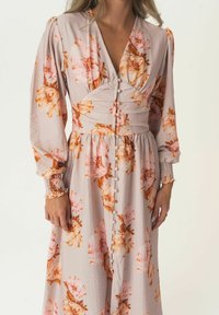 Lange bloemenjurk met roze en oranje bloemenpatronen, lichte stof, knoopdetails aan de voorkant en smockmanchetten.