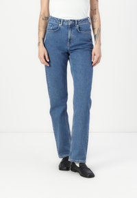 Jeans azul de talle alto y pierna recta, fabricados en denim. Cuenta con cinco bolsillos, presillas para el cinturón y un cierre clásico de botón. Textura suave.