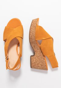 Sandali con zeppa in suede giallo, con punta aperta, design a fascia incrociata e piattaforma in sughero. Presentano un accento arancione attorno al tallone.